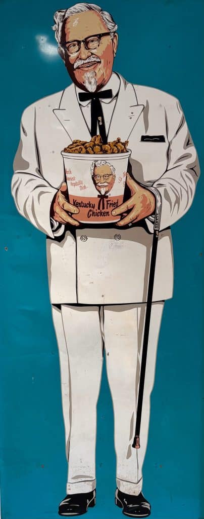 Cartoon illustration of Colonel Harland Sanders holding a bucket of Kentucky Fried Chicken.